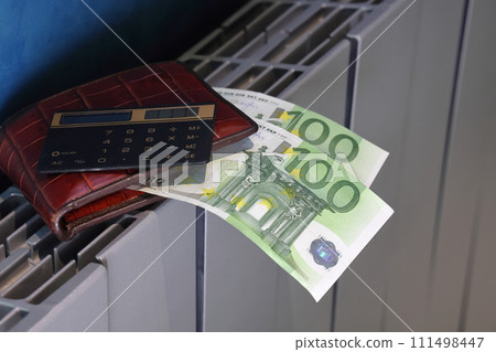 Calculator, wallet and banknotes with 100 euros lie on the radiator of the heating system 111498447