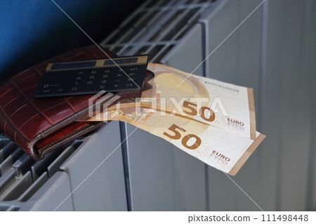 Calculator, wallet and banknotes with 100 euros lie on the radiator of the heating system 111498448