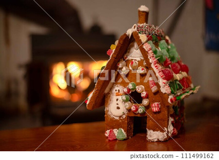 Gingerbread house with holiday candy decoration by cozy fireplace 111499162
