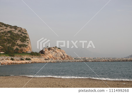 Storm at sea on Cleopatra Beach, foam waves against the background of the historic mountain, Alanya, November 2021. Storm at sea on Cleopatra Beach, foam waves against the background of the historic mountain, Alanya, November 2021. 111499268
