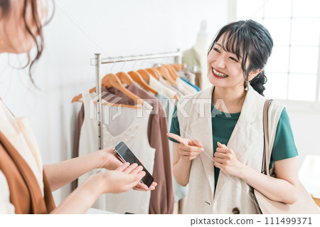 A woman and a shop clerk shopping using smartphones, smartphone payments, and online payments A woman and a shop clerk shopping using smartphones, smartphone payments, and online payments 111499371