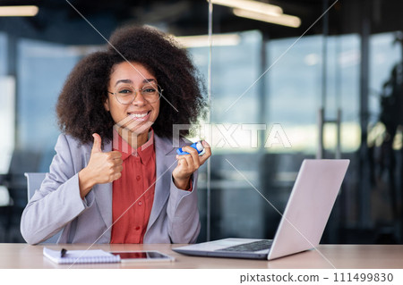 Relieved latino lady in business suit showing thumb um gesture and holding asthmatic aerosol while sitting in cabinet. Smiling administrator feeling better after dealing with bronchial disease attack. Relieved latino lady in business suit showing thumb um gesture and holding asthmatic aerosol while sitting in cabinet. Smiling administrator feeling better after dealing with bronchial disease attack. 111499830