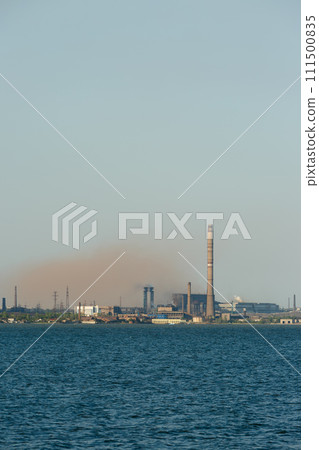 Industrial skyline dominated by a metallurgical plants tall chimneys emitting smoke over a body of water, symbolizing industrial pollution and eco awareness issues. 111500835
