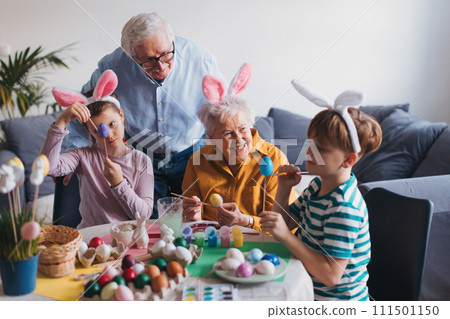 Grandmother with little kids decorating easter eggs at home. Tradition of painting eggs with brush and easter egg dye. Grandmother with little kids decorating easter eggs at home. Tradition of painting eggs with brush and easter egg dye. 111501150