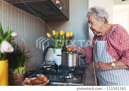 Senior woman preparing traditional easter meals for family, boiling eggs. Recreating family traditions and customs. 111501162