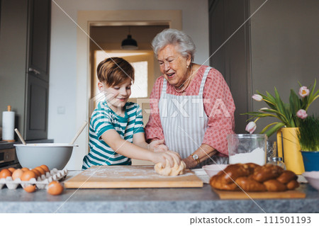 Grandmother with grandson preparing traditional easter meals, kneading dough for easter cross buns. Passing down family recipes, custom and stories. 111501193