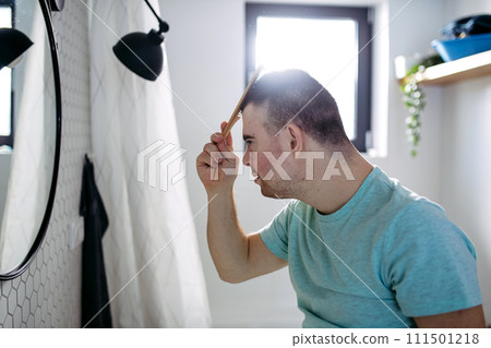 Young man with down syndrome in bathroom, combing his hairs. Young man with down syndrome in bathroom, combing his hairs. 111501218
