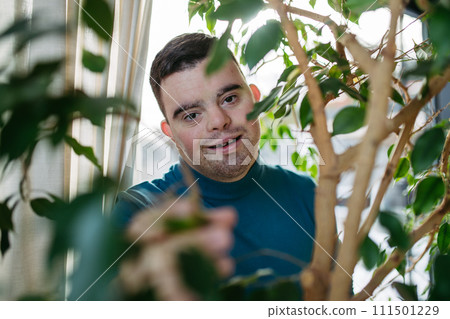 Portrait of young man with Down syndrome in the middle of indoor plants. 111501229
