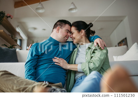 Portrait of young man with Down syndrome with his mother at home, holding, touching with foreheads. Concept of love and parenting disabled child. Banner with copyspace. 111501230