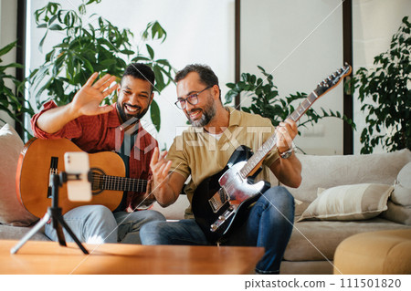 Best friends, musician jamming together, making video on social media. Playing music on guitar together at home for fans. Concept of male friendship, bromance. 111501820