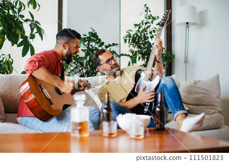 Best friends, musician jamming together. Playing music on guitar together, having beer and fun. Concept of male friendship, bromance. 111501823