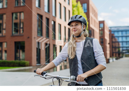 Beautiful middle-aged woman commuting through the city by bike. Female city commuter traveling from work by bike after long workday. Beautiful middle-aged woman commuting through the city by bike. Female city commuter traveling from work by bike after long workday. 111501830