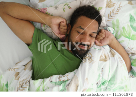 Top view of man waking up in bed, stretching arms, smiling in the morning. 111501878