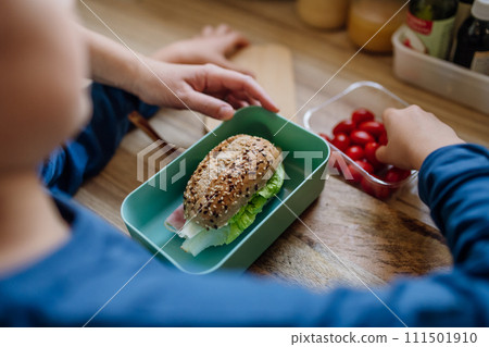 Boy helping mother to make school lunch in the kitchen. Preparing healthy snack for school. 111501910