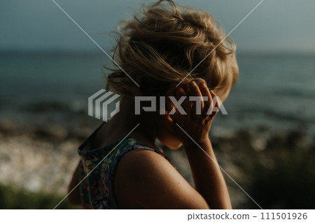 Side view of small girl with blonde hair standing at beach looking at sea. Side view of small girl with blonde hair standing at beach looking at sea. 111501926