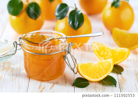 Close-up of glass jar with orange jam on white table with orange slices, selective focus. 111502553