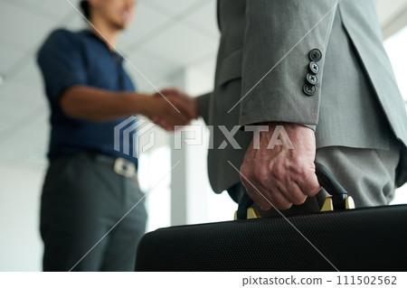 Hand of successful broker or agent holding briefcase while standing in front of camera during handshake with his client or business partner 111502562