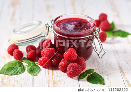 Glass jar of raspberry jam with fresh berries on a white wooden table. 111502563