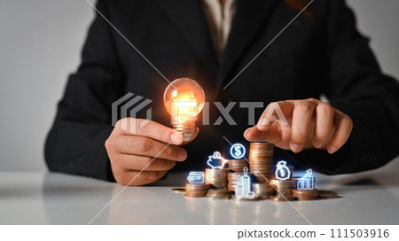 Businesswoman holding glowing light bulb near with stack of coins. Saving money and financial growth concept 111503916