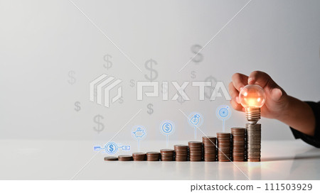 Hand holding a glowing light bulb over coin stack. Saving money for investing in fund and business ideas concept Hand holding a glowing light bulb over coin stack. Saving money for investing in fund and business ideas concept 111503929