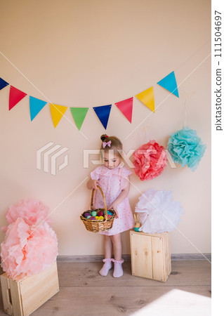 Cute little girl wearing pink dress holding basket with painted Easter eggs Cute little girl wearing pink dress holding basket with painted Easter eggs 111504697