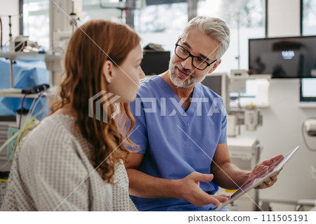 Doctor showing teenage patient MRI scan on tablet, discussing test result in emergency room. 111505191
