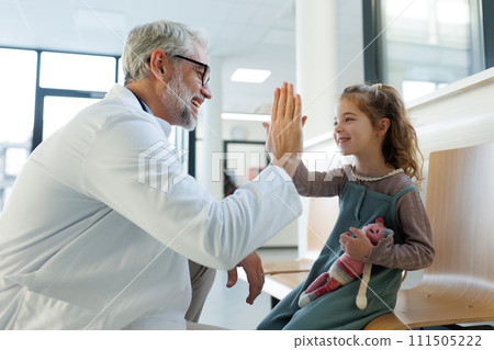 Friendly pediatrician giving high five to little patient. Cute preschool girl in greeting doctor in hospital corridor. 111505222