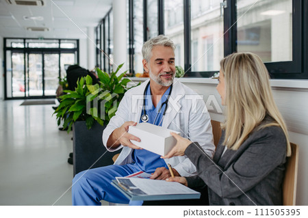 Pharmaceutical sales representative presenting new medication to doctor in medical building, holding box with medication samples. Pharmaceutical sales representative presenting new medication to doctor in medical building, holding box with medication samples. 111505395