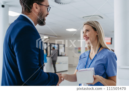 Pharmaceutical sales representative talking with doctor in medical building. Ambitious male sales representative presenting new medication on tablet. 111505470
