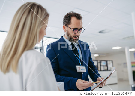 Pharmaceutical sales representative talking with doctor in medical building. Ambitious male sales representative presenting new medication on tablet. 111505477