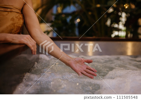 Close up of woman standing by hot tub, splashing water, enjoying wellness weekend in spa. Close up of woman standing by hot tub, splashing water, enjoying wellness weekend in spa. 111505548