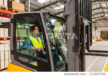 Female warehouse worker driving forklift. Warehouse worker preparing products for shipmennt, delivery, checking stock in warehouse. Female warehouse worker driving forklift. Warehouse worker preparing products for shipmennt, delivery, checking stock in warehouse. 111505740