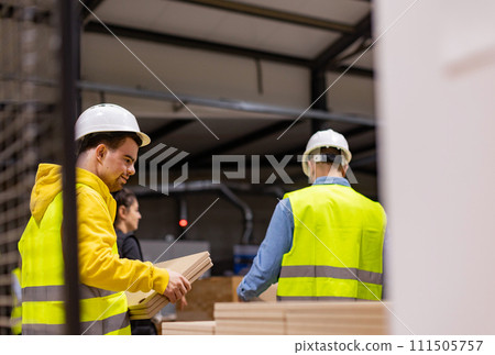 Young man with Down syndrome working in modern factory, colleague teaching him about his job, showing process. Concept of workers with disabilities, support in workplace. 111505757