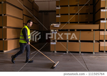 Portrait of young man with Down syndrome sweeping the floor, working in factory, warehouse. Concept of workers with disabilities, support in workplace. 111505764