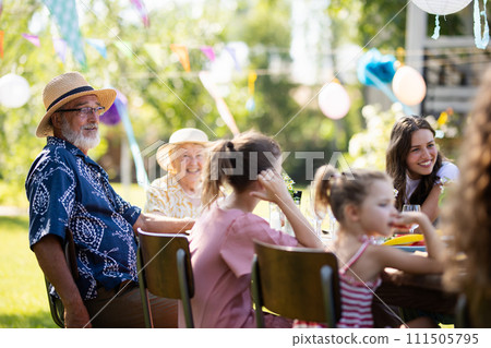 Family chatting, and having fun at party table during summer garden party. Grandfather sitting at head of table. 111505795