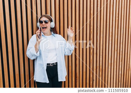 Closeup portrait of a lovely young girl listening to music through wireless earphones on wooden rustic background. Music lover enjoying music. Woman record voice by mobie dictaphone 111505910