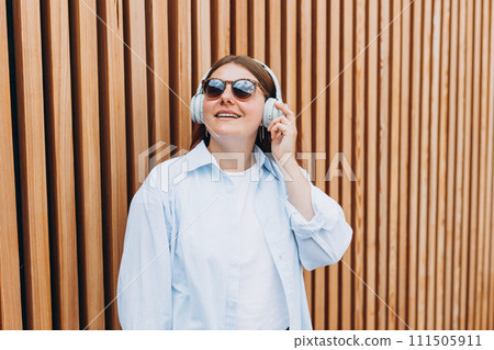 Closeup portrait of a lovely young woman listening to music through wireless earphones on wooden rustic background. Music lover enjoying music. Closeup portrait of a lovely young woman listening to music through wireless earphones on wooden rustic background. Music lover enjoying music. 111505911