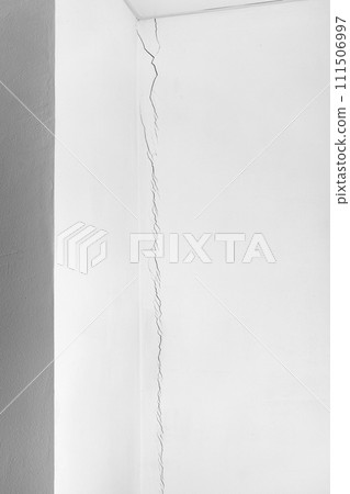 Deep crack in the white wall from floor to ceiling. Problems of construction and repair. Deep crack in the white wall from floor to ceiling. Problems of construction and repair. 111506997