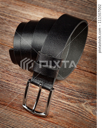 Black leather belt on a wooden brown background. Black leather belt on a wooden brown background. 111507002