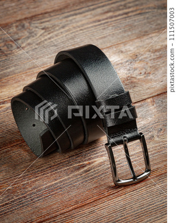 Black leather belt on a wooden brown background. 111507003