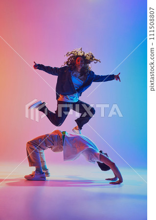 Acrobatic dance pair, woman jumping and man in handstand, against gradient studio background in neon light, filter. 111508807