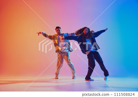 Dynamic photo of two fashion dressed people, dancing in motion against gradient studio background in neon light, filter. Dynamic photo of two fashion dressed people, dancing in motion against gradient studio background in neon light, filter. 111508824