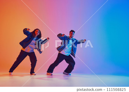 Street style. Two hip-hop dancers, man and woman, in motion against gradient studio background in neon lighting, filter. 111508825