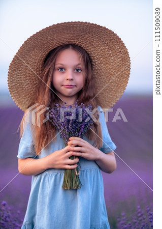 Girl lavender field in a blue dress with flowing hair in a hat stands in a lilac lavender field Girl lavender field in a blue dress with flowing hair in a hat stands in a lilac lavender field 111509089