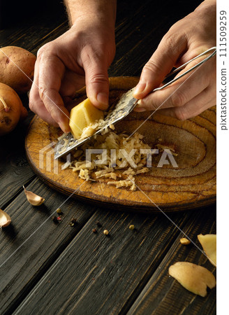 Chef is preparing potato pancakes on the kitchen table. Close-up of a cook hands grating potatoes Chef is preparing potato pancakes on the kitchen table. Close-up of a cook hands grating potatoes 111509259