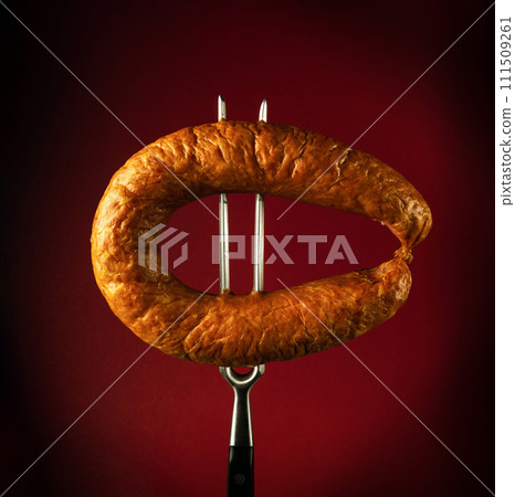 Sausage on a fork in a restaurant. Delicious and fast food concept with Munich sausage on a red background Sausage on a fork in a restaurant. Delicious and fast food concept with Munich sausage on a red background 111509261