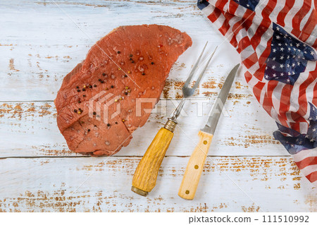 Preparation raw beef steak on table in honor American holidays is accompanied by display of USA flag Preparation raw beef steak on table in honor American holidays is accompanied by display of USA flag 111510992