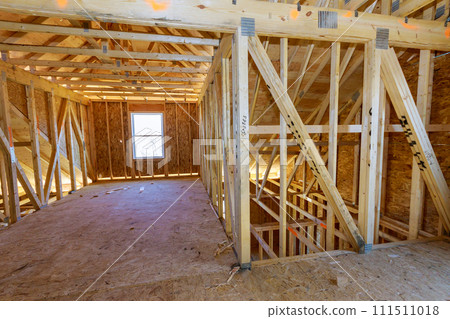 An unfinished house with wooden framing beams in construction work progress view An unfinished house with wooden framing beams in construction work progress view 111511018