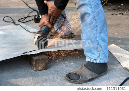 Worker using a electric grinder to cut a Zinc steel while sparks are flying. 111511081