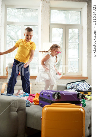 Two kids, boy and girl jumping of joy and happiness on bed and having fun when preparing for family trip. Children's summer camp. Two kids, boy and girl jumping of joy and happiness on bed and having fun when preparing for family trip. Children's summer camp. 111514322